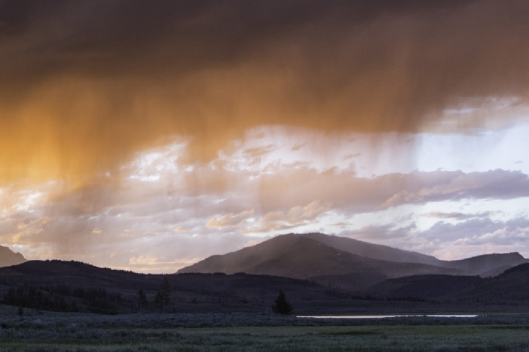 A cloudy sky with rain falling over a mountainous landscape. Text on the left reads "Precipitation Essential Climate Variable (ECV) Factsheet" with logos at the bottom.